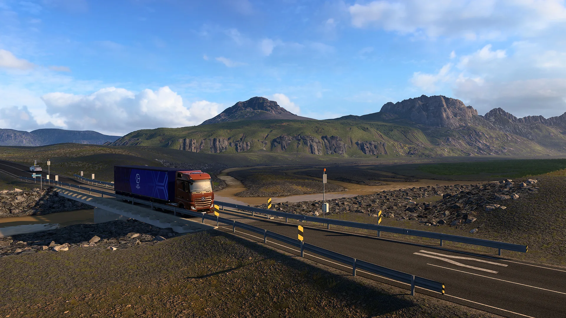 A truck crosses a lava field on an Iceland road, with mountains behind