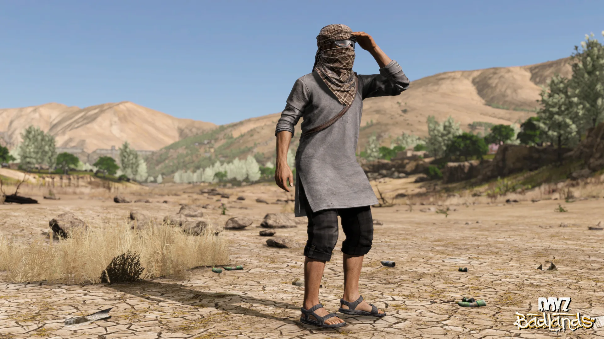 A survivor in a shemagh, tunic and sandals shading his eyes on a cracked, sunbaked plain